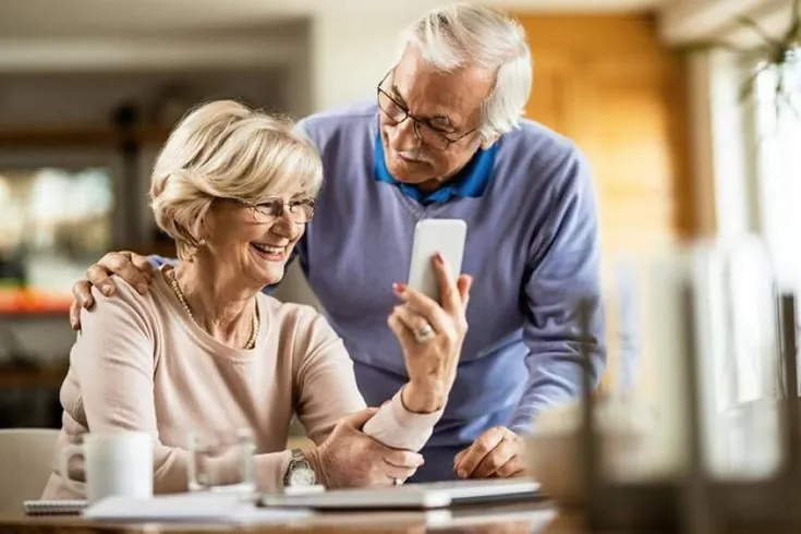 Casal de pessoas idosas consultando um celular, em foto ilustrativa